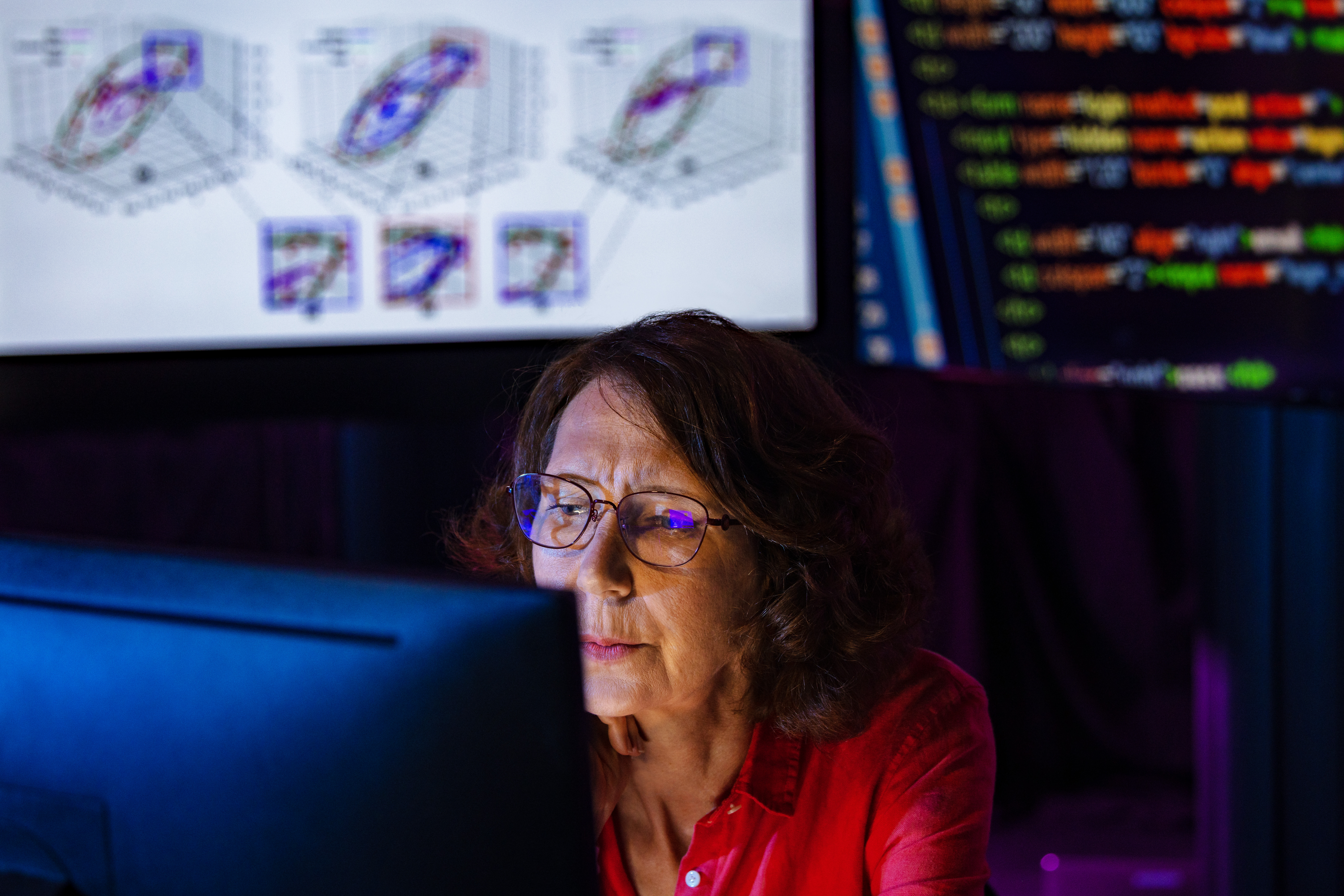A researcher sits in front of a computer with lines of code in the background