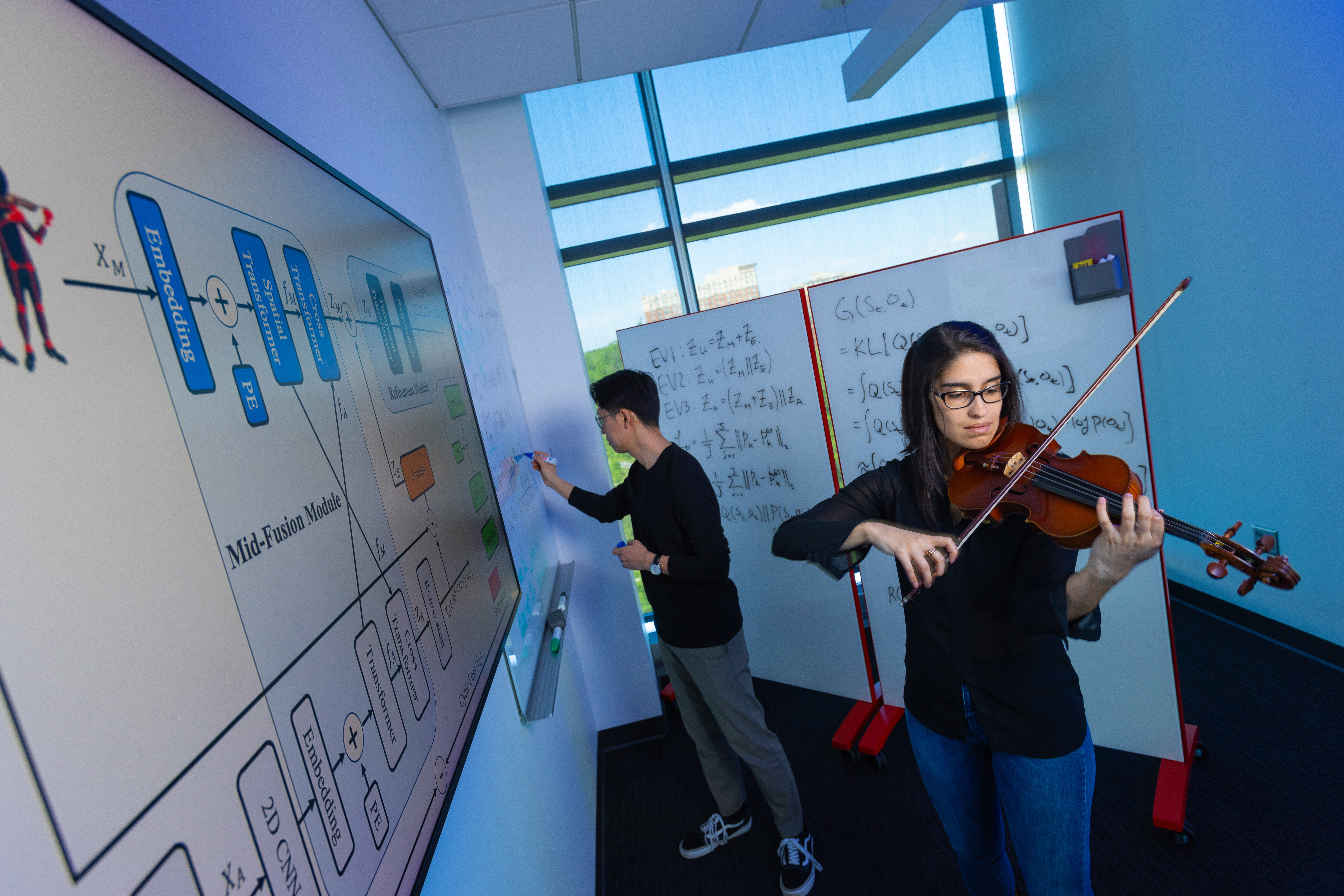 A woman plays the violin while a man stands at a dry erase board