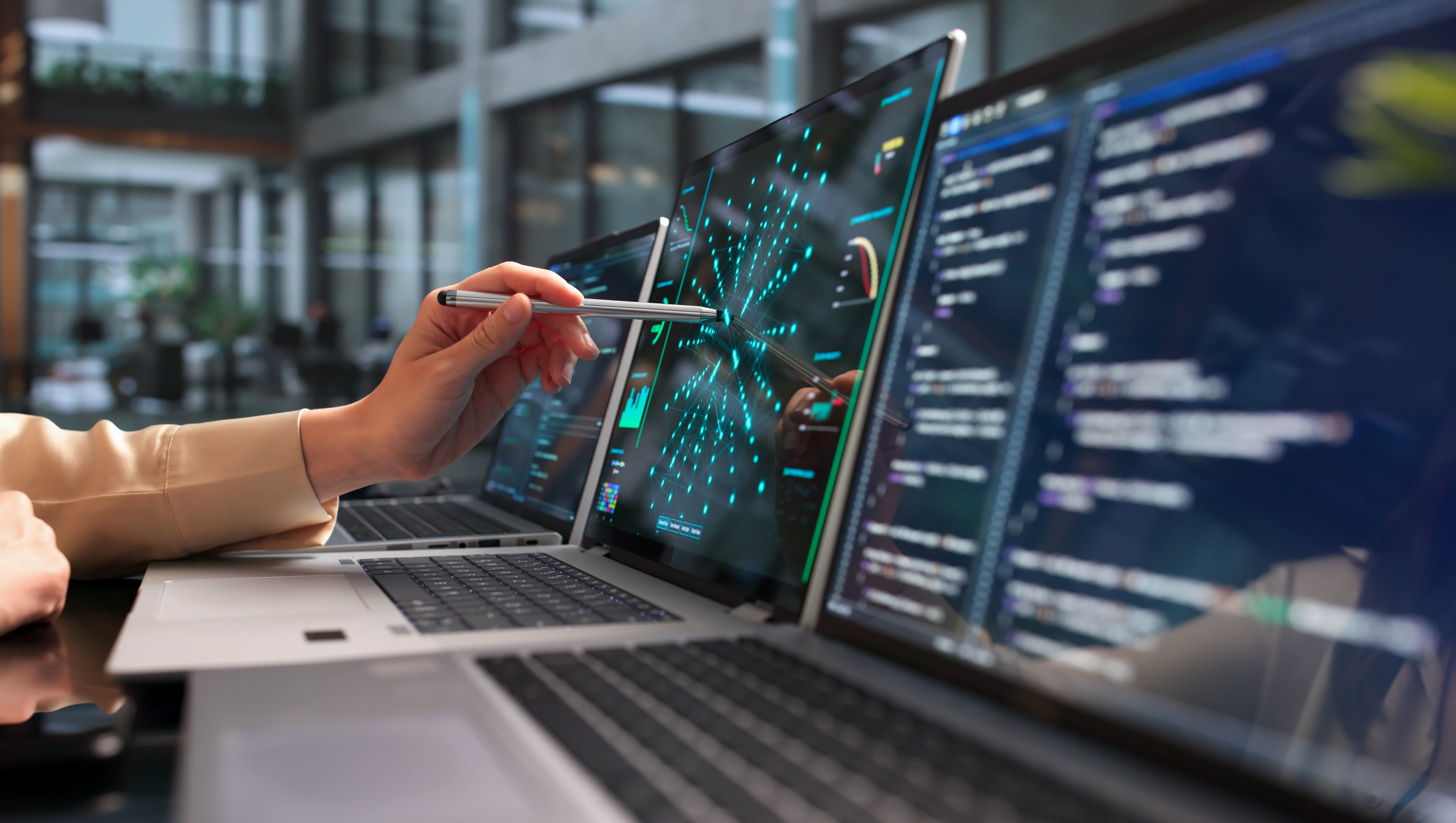 A person holding a stylys to a laptop screen with a laptop to their left and right.